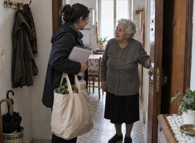 Operatrice domiciliare consegna la spesa a una donna anziana nella sua abitazione.