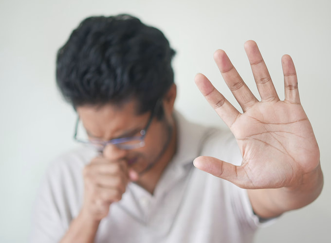 Persona che tossisce con la mano alzata in primo piano, immagine associata ai sintomi della tosse cronica e ai disturbi respiratori.